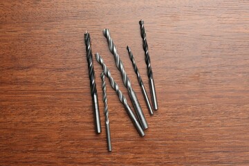 Many drill bits on wooden table, flat lay