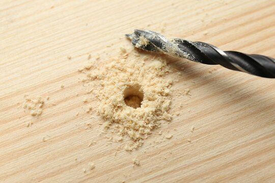 Drill bit and sawdust on holed wooden surface, closeup