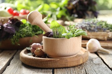 Different aromatic herbs, mortar with pestle and spices on wooden table, closeup