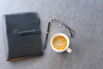 ミルクをたっぷり入れたコーヒー、カフェ・ラッテを飲みながら、システム手帳でデスクワーク中のイメージ
