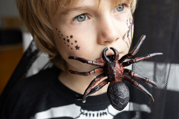 Close-up of the boy's face, holding a large spider in his teeth. the child looks away. Halloween holiday. trick or treat