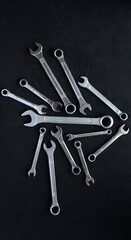 Variety size chrome plated wrenches from one set laid out on black surface. Vertical stock photo for mechanical backgrounds
