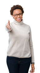 Fototapeta premium Young beautiful african american woman wearing glasses over isolated background smiling friendly offering handshake as greeting and welcoming. Successful business.