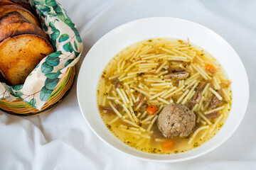 Beef broth with noodle, liver dumpling and cerrot soup in white plate, toasted fried bread.