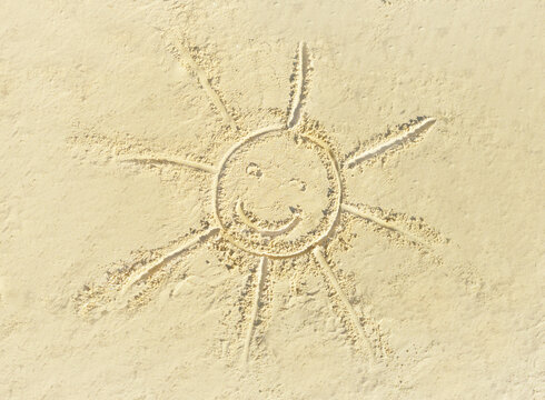 An engraving drawing in light yellowish sea sand of a smiling smiley sun face. Tropical island on clean sand with free areas for text. Photographed from above in close-up. Suitable vacation postcards