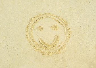 An engraving drawing in light yellowish sea sand of a smiling smiley face. Tropical island on clean sand with free areas for text. Photographed from above in close-up. Suitable for vacation postcards