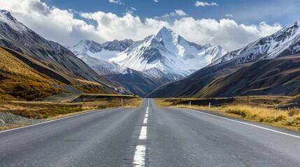 Naklejka premium Mountain Road Journey - A long, straight road cutting through a mountain pass, the snow-capped peaks towering above and a blue sky with fluffy clouds.