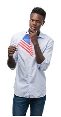 Young african american man holding USA flag serious face thinking about question, very confused idea