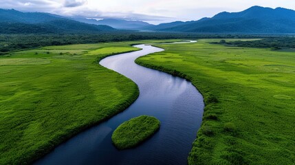 Aerial view of a winding river flowing through lush green fields with mountains in the background at sunset.