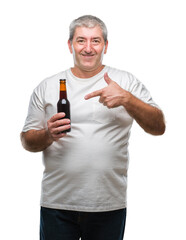 Handsome senior man drinking beer bottle over isolated background very happy pointing with hand and finger