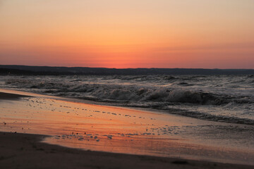 The bright pink sunset sky is reflected in the sea waves lying on the dark sandy coast