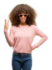 African american woman wearing pink sunglasses showing and pointing up with fingers number three while smiling confident and happy.