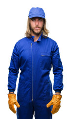 Young handsome mechanic man with long hair over isolated background with serious expression on face. Simple and natural looking at the camera.