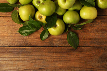 Ripe green apples with leaves on wooden table, flat lay. Space for text