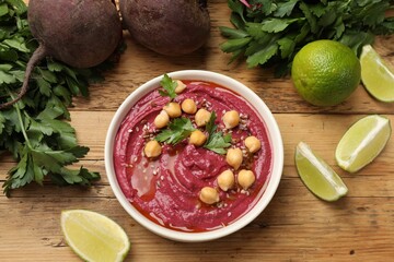 Tasty beet hummus with chickpeas in bowl and fresh ingredients on wooden table, flat lay
