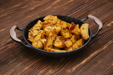 Baked potato wedges with spices, herbs and garlic on wooden table