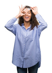 Beautiful young hispanic woman wearing glasses with happy face smiling doing ok sign with hand on eye looking through fingers