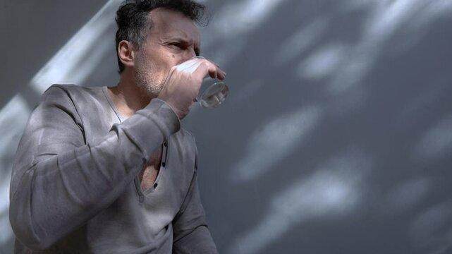 Adult male deeply worried, taking antidepressant and resting on the wall. The soft lighting and shadows create a reflective and somber mood. Copy space.