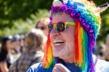 Man smiling at a pride event wearing rainbow sunglasses and hat