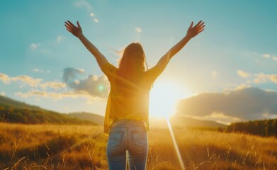 A woman is standing in a field with her arms raised, looking up at the sun. Concept of joy and...