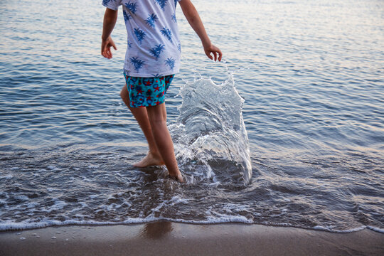 Child playing with splashes of water in the sea at sunset