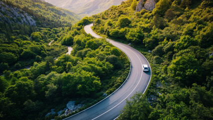 Car Driving on a Curvy Mountain Road Surrounded by Lush Green Forest
