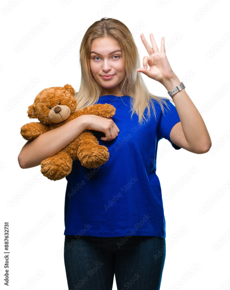 Poster Young caucasian woman holding cute teddy bear over isolated background doing ok sign with fingers, excellent symbol