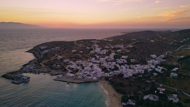 A breathtaking aerial view of Stavros, Donousa, Greece, showcasing a picturesque coastal town nestled amidst a rugged landscape, with the sun setting over the Aegean Sea.