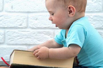 Funny portrait of little baby looks at a books. Intellectual development of newborns.