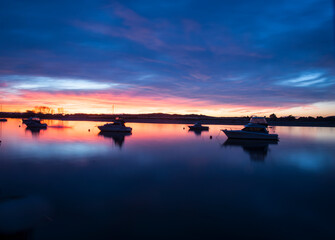 Intense sunset colours and reflections in long exposure with boats slightly blurred in bay