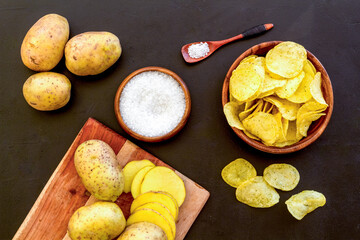 Homemade low calorie potato chips with raw potatoes on board, top view