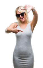 Young beautiful blonde woman wearing sunglasses over isolated background smiling making frame with hands and fingers with happy face. Creativity and photography concept.