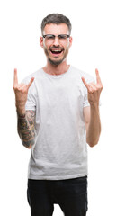 Young tattooed adult man shouting with crazy expression doing rock symbol with hands up. Music star. Heavy concept.