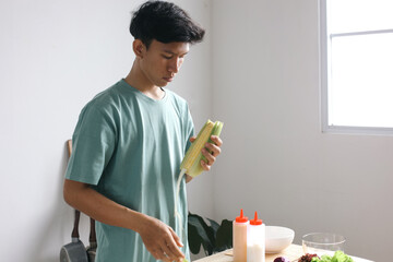 Asian young man making salad, peeling off the corn in the kitchen