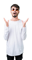 Naklejka premium Young handsome man wearing sunglasses over isolated background crazy and mad shouting and yelling with aggressive expression and arms raised. Frustration concept.