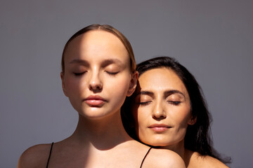 Beauty portrait of two attractive young women with clean healthy skin and hair. Charming models with natural makeup on a gray isolated background. Cosmetology and spa treatments. Skin care concept.