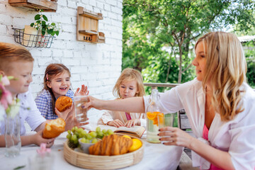 Young mother and three children are having lunch on terrace of house.