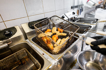 A commercial kitchen deep fryer cooks chicken pieces, highlighting professional food preparation