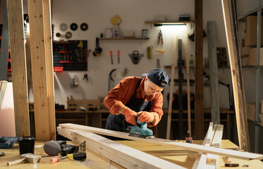 carpenter sanding wood plank using sander machine in workshop in carpentry shop