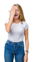 Fototapeta premium Beautiful young woman wearing casual white t-shirt over isolated background covering one eye with hand with confident smile on face and surprise emotion.