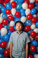 Obraz premium A young man in a blue shirt stands amidst a sea of red, white, and blue balloons