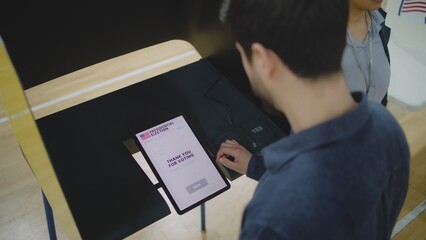 High angle of man making choice and voting for presidential candidate in voting booth using tablet...