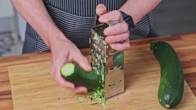 Front view of man hand rubbing the zucchini on metal grater. Close-up.