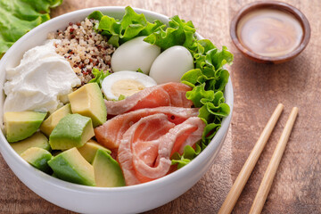 Salmon quinoa bowl with greens and vegetable on the wooden table. Balance in bowl.  Top view.