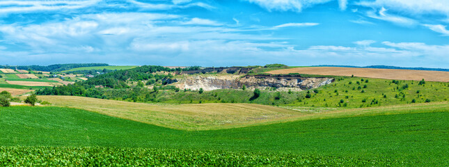 Panoramic summer view of hills, field, forest and blue sky with clouds on a sunny day. Career.