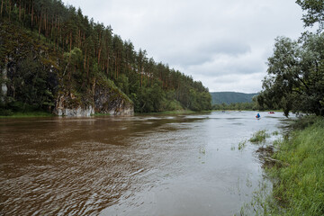 The tranquil river flows gently through a beautiful scenery with trees, mountains, and cloudy...