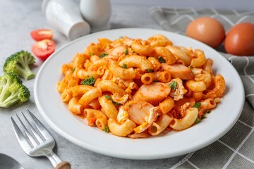 Stir fried macaroni with tomato sauce and sausage with egg   in a white plate with fork and spoon,