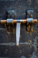 A close-up view of a rusty metal door bolt secured on a weathered black wooden door with antique features