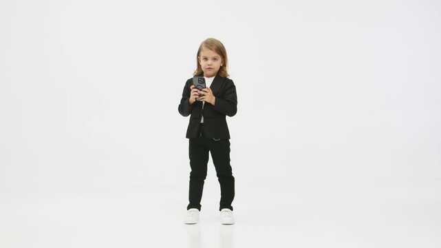 Concept of business, deal and modern technology. Little business girl on a white background in the studio presses her mobile phone and shows a &ldquo;super&rdquo; gesture of approval.