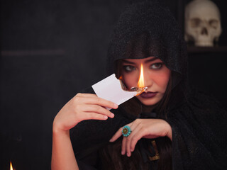 Obraz premium Beautiful serious mysterious woman in the darkness holding the burning tarot cards for the fortune teller read future.